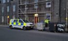 A police officer stands guard at flats on Bedford Road in Aberdeen. The building is covered in scaffolding. A police van is also parked outside.