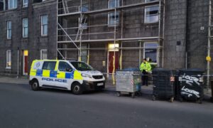 A police officer stands guard at flats on Bedford Road in Aberdeen. The building is covered in scaffolding. A police van is also parked outside.