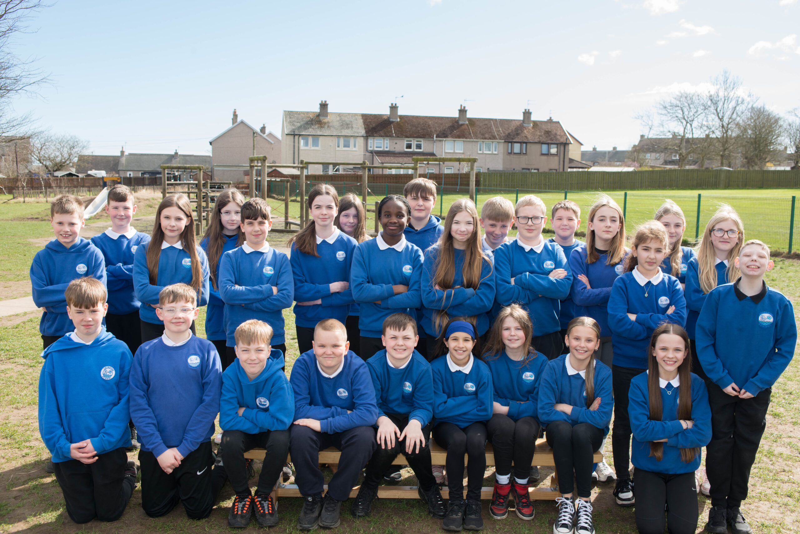 Three rows of pupils in the playground in blue sweatshirts.