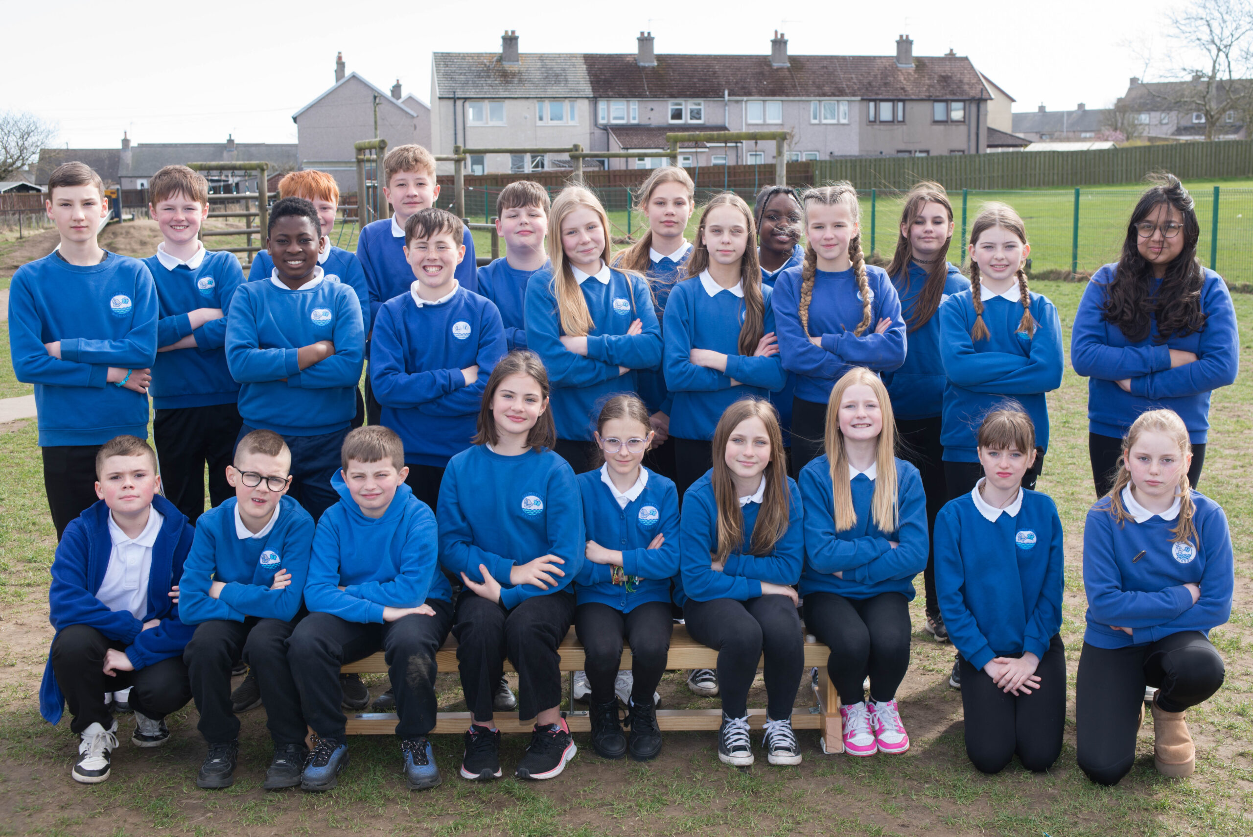 Three rows of pupils in the playground in blue sweatshirts.