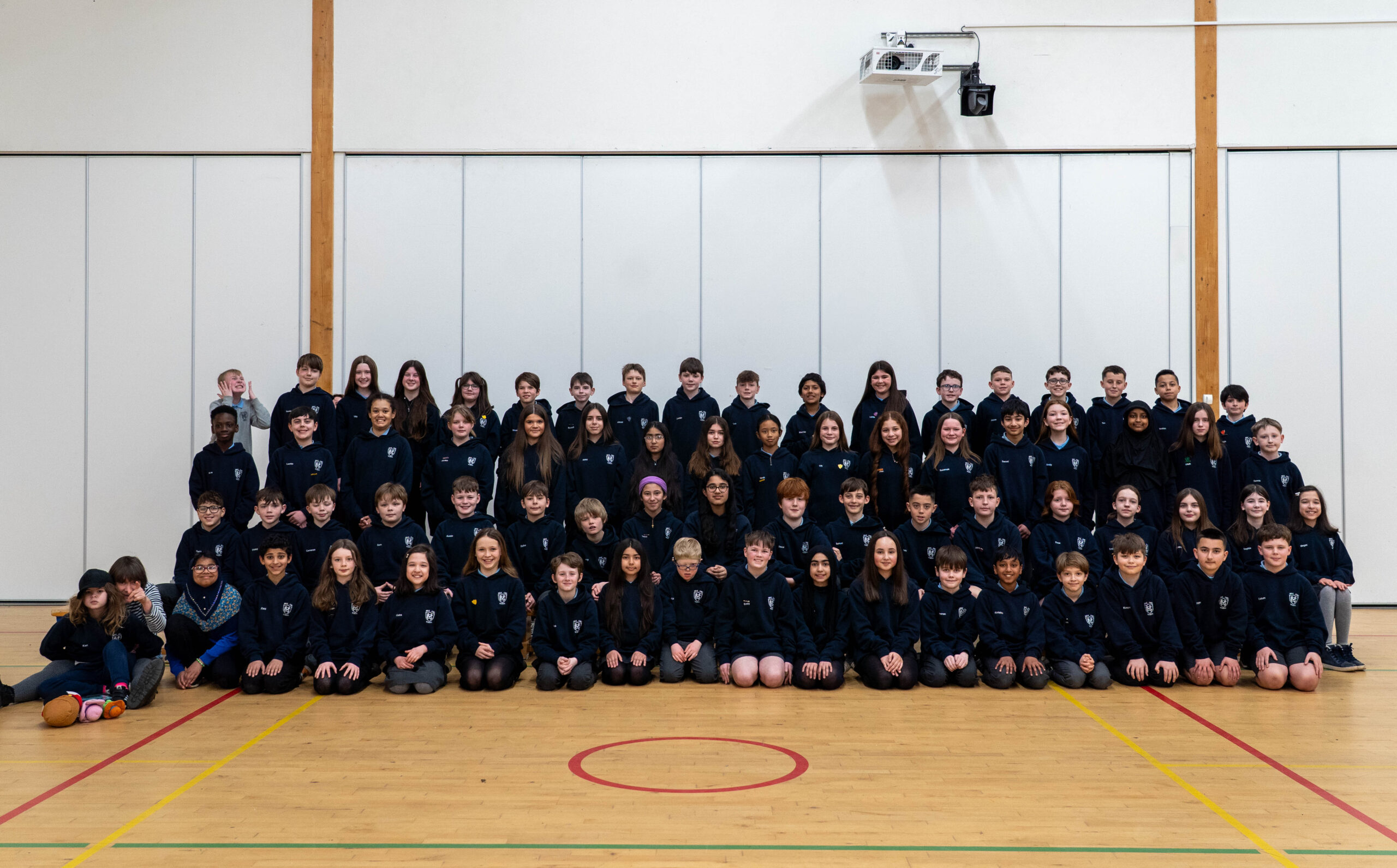 Four rows of pupils in black tops in a games hall.