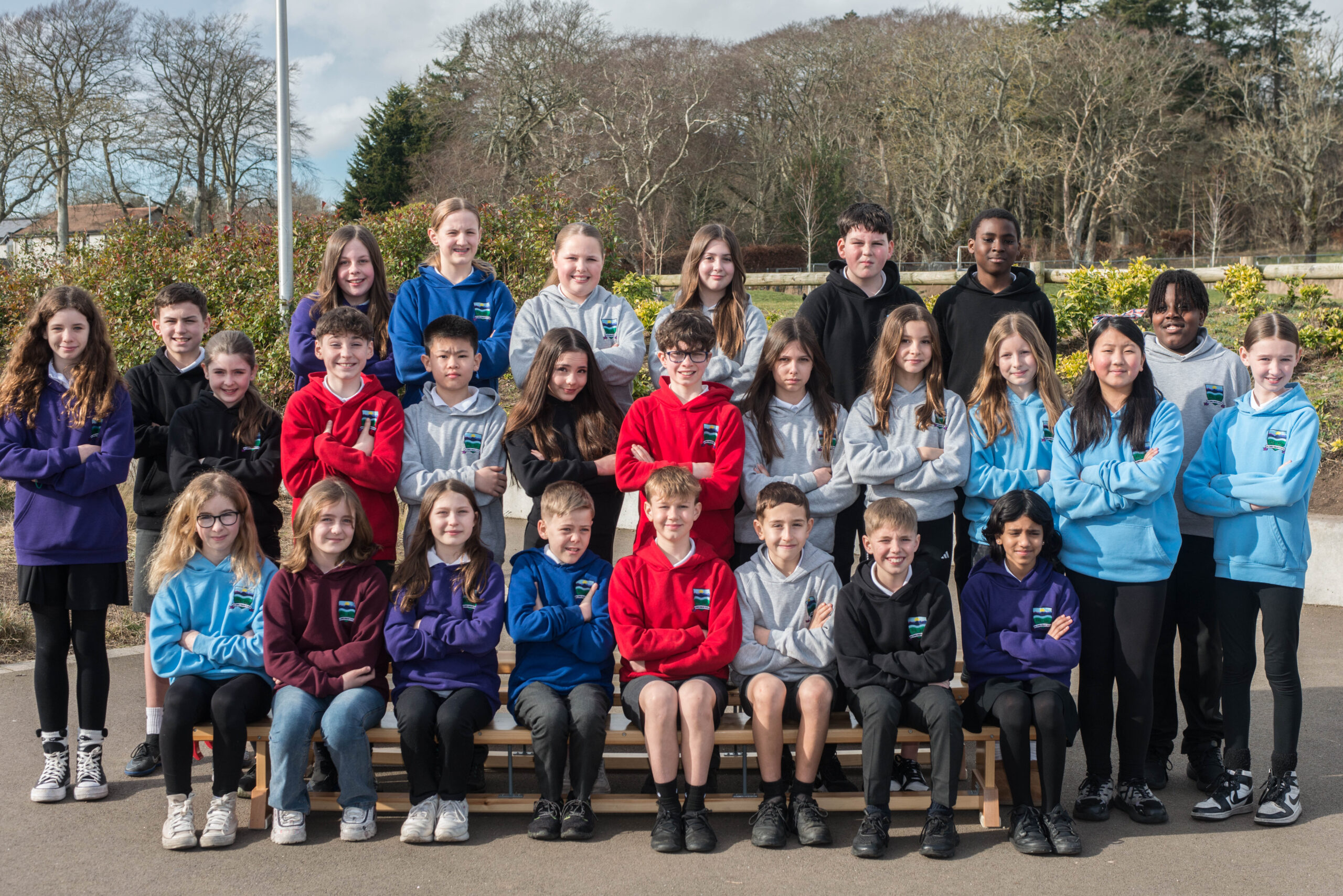 Three rows of pupils on benches outside in various colours of school tops.