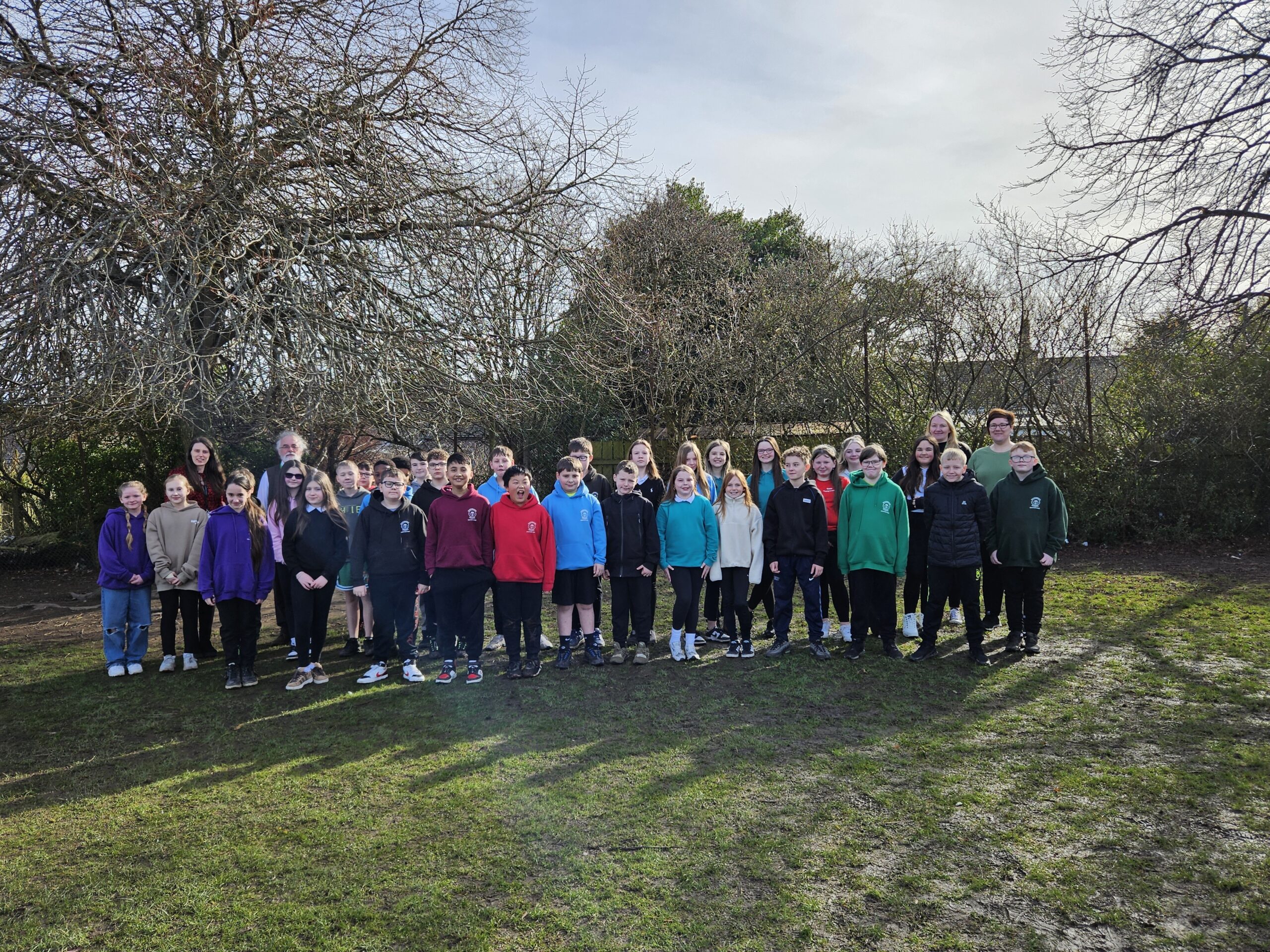 A group of pupils standing on grass with trees behind them.