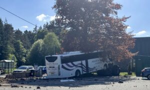 The coach rests against a tree - and on top of a c car that had been parked in the car park. A stone wall, which the bus punched through, is to the left. Debris can be seen scattered across the car park in Dinnet.