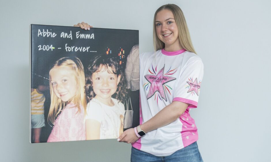 Emma Whitton holding up canvas picture showing herself and Abbie as children. 