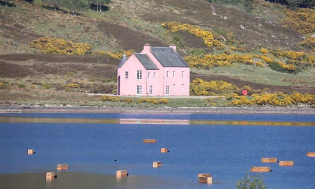 Coffins floating on Loch Glass, with a large pink house in the background.