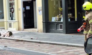 smashed masonry on the pavement to the left of the picture as a firefighters stands on the right.