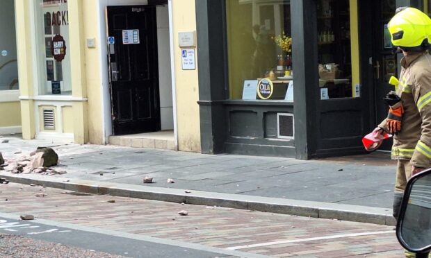 smashed masonry on the pavement to the left of the picture as a firefighters stands on the right.