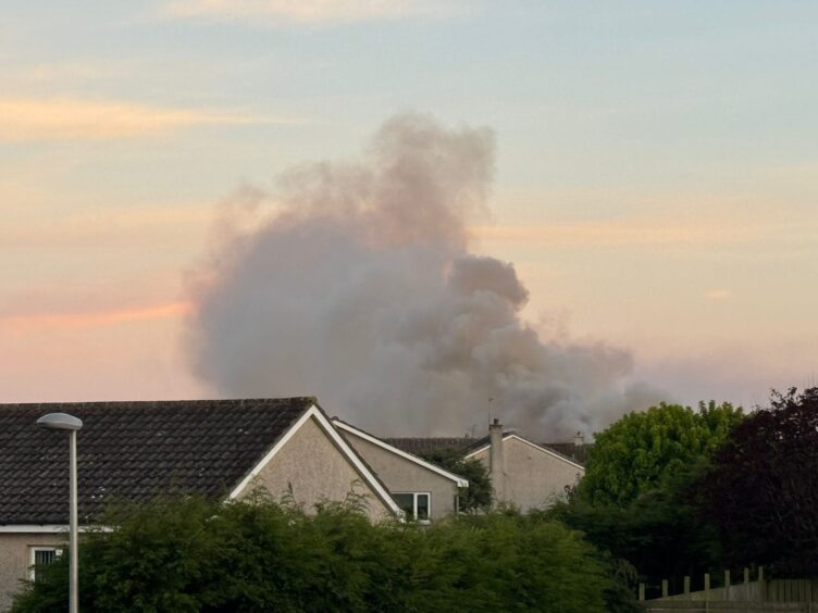 Large plume of smoke rising beyond houses.