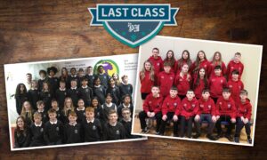 Two class photos lying flat on a wooden surface with a Last class logo in the shape of a school badge above them. Colour pic.