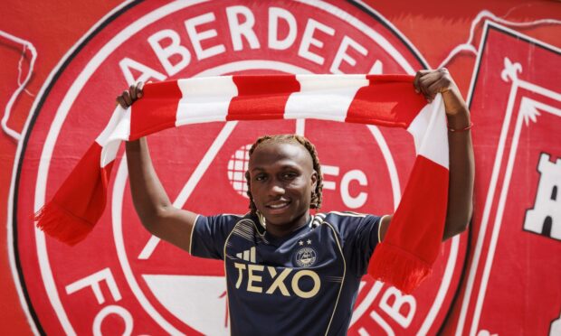 New Aberdeen signing Emmanuel Gyamfi raises a club scarf.