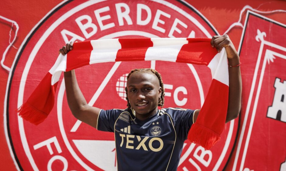 New Aberdeen signing Emmanuel Gyamfi raises a club scarf.