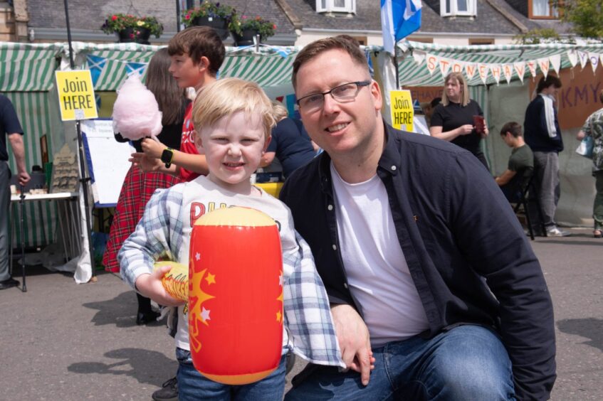 A man and a child holding an inflatable hammer at the Feein' Market in Stonehaven.