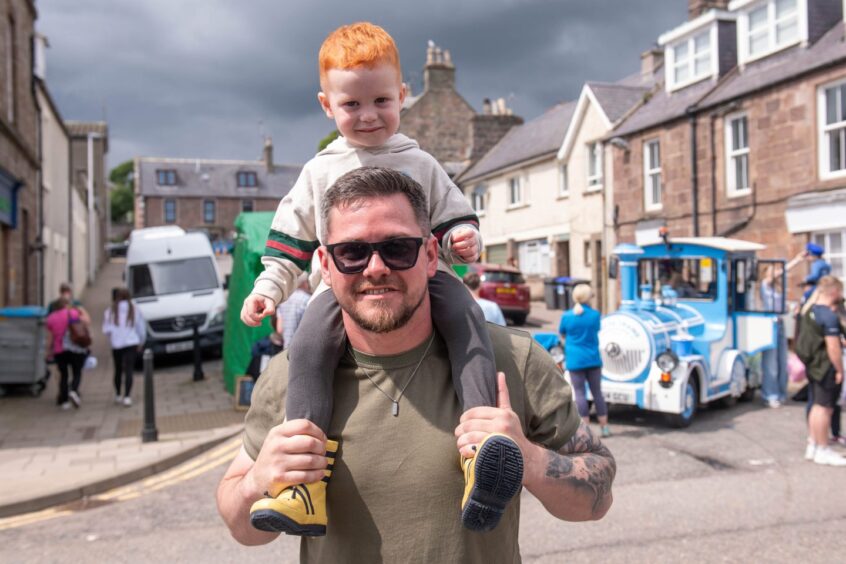 A child sits on a man's shoulders. The Stonehaven Land Train is in the background.