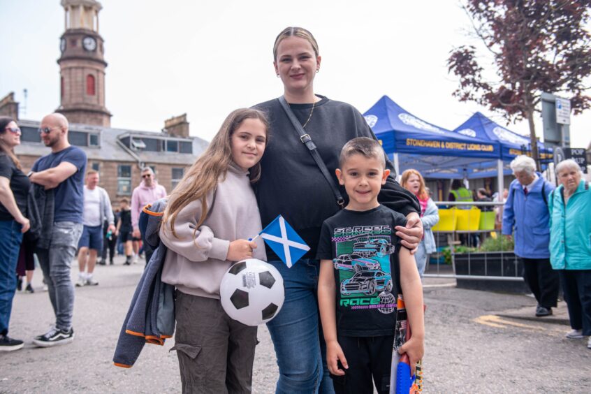 Two children and an adult. One of the children is holding a football and a Saltire.
