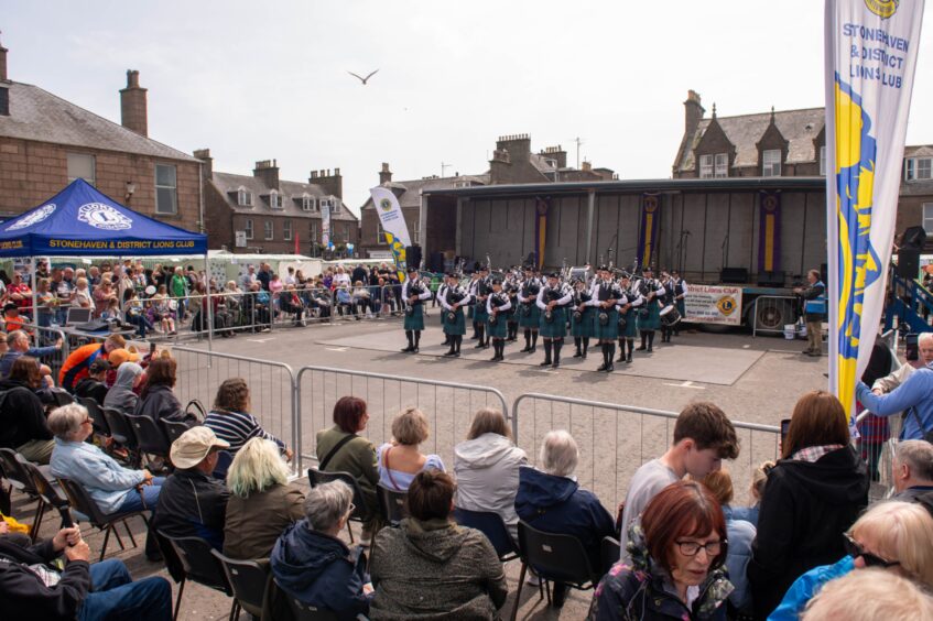 The pipe band behind barriers as a seated crowd looks on.