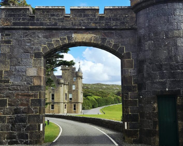 A Scottish baronial-style stately home viewed through a stone arch at the entrance to the estate.