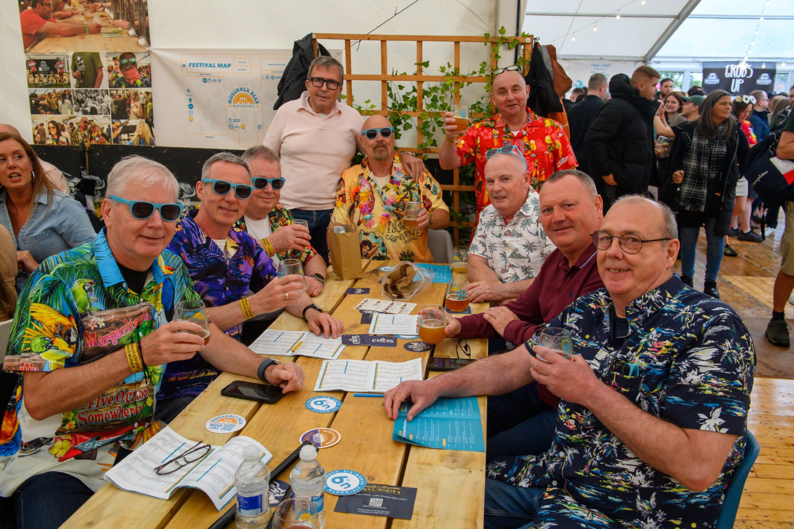 Nine men sit around a table with beer