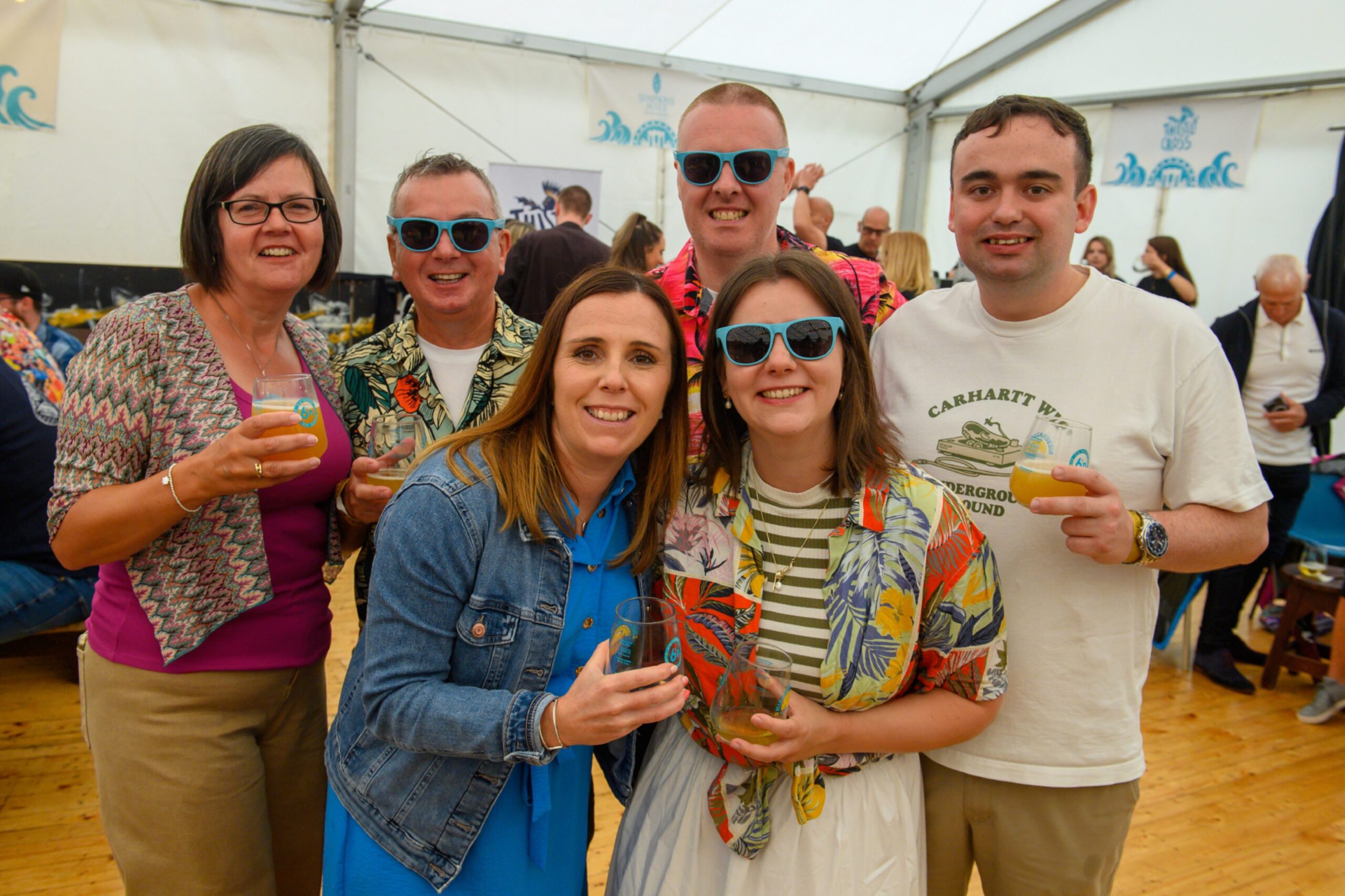 Six people pose with beer in hand, three of them wearing sunglasses