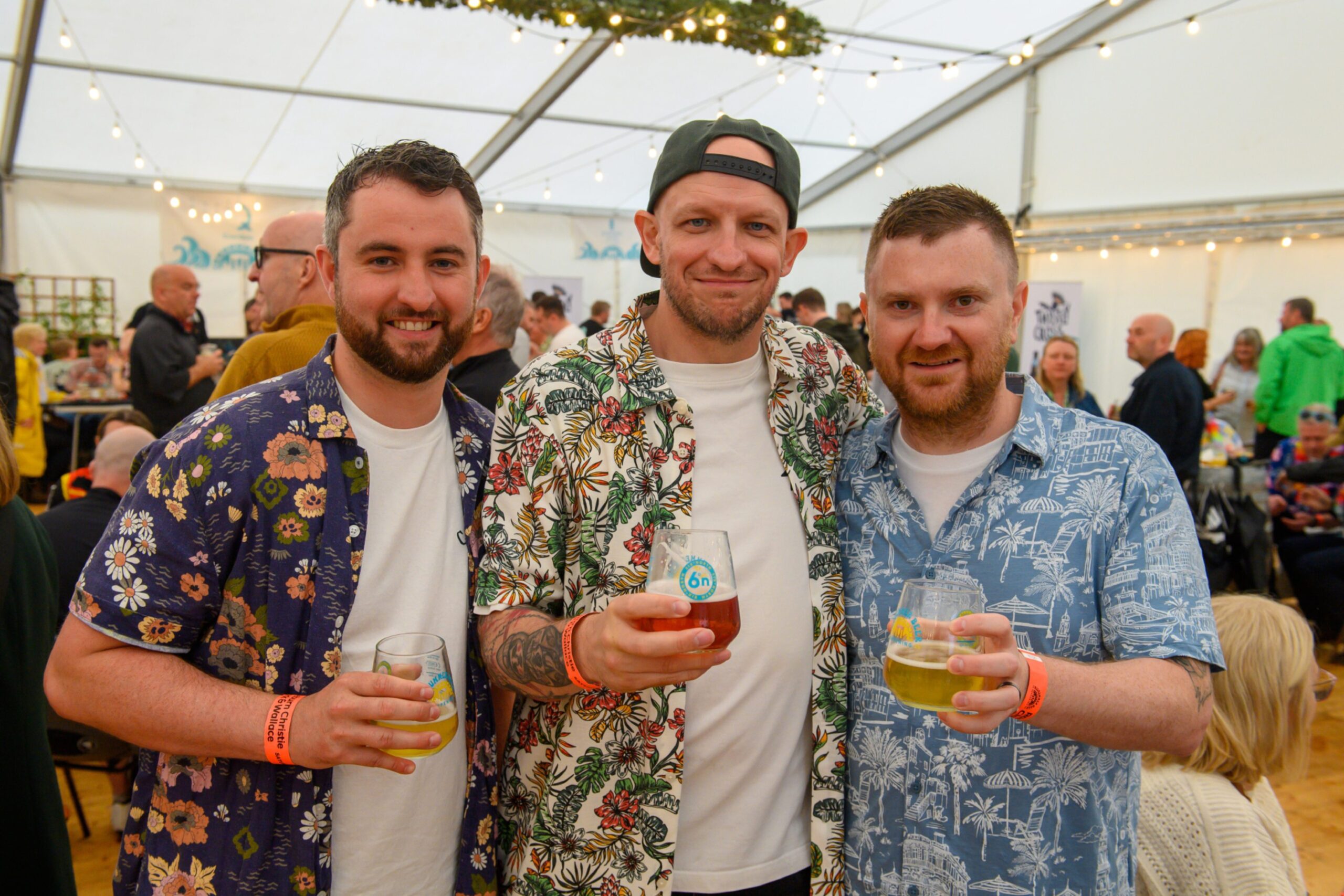Three men in Hawaiian shirts pose with beer in hand