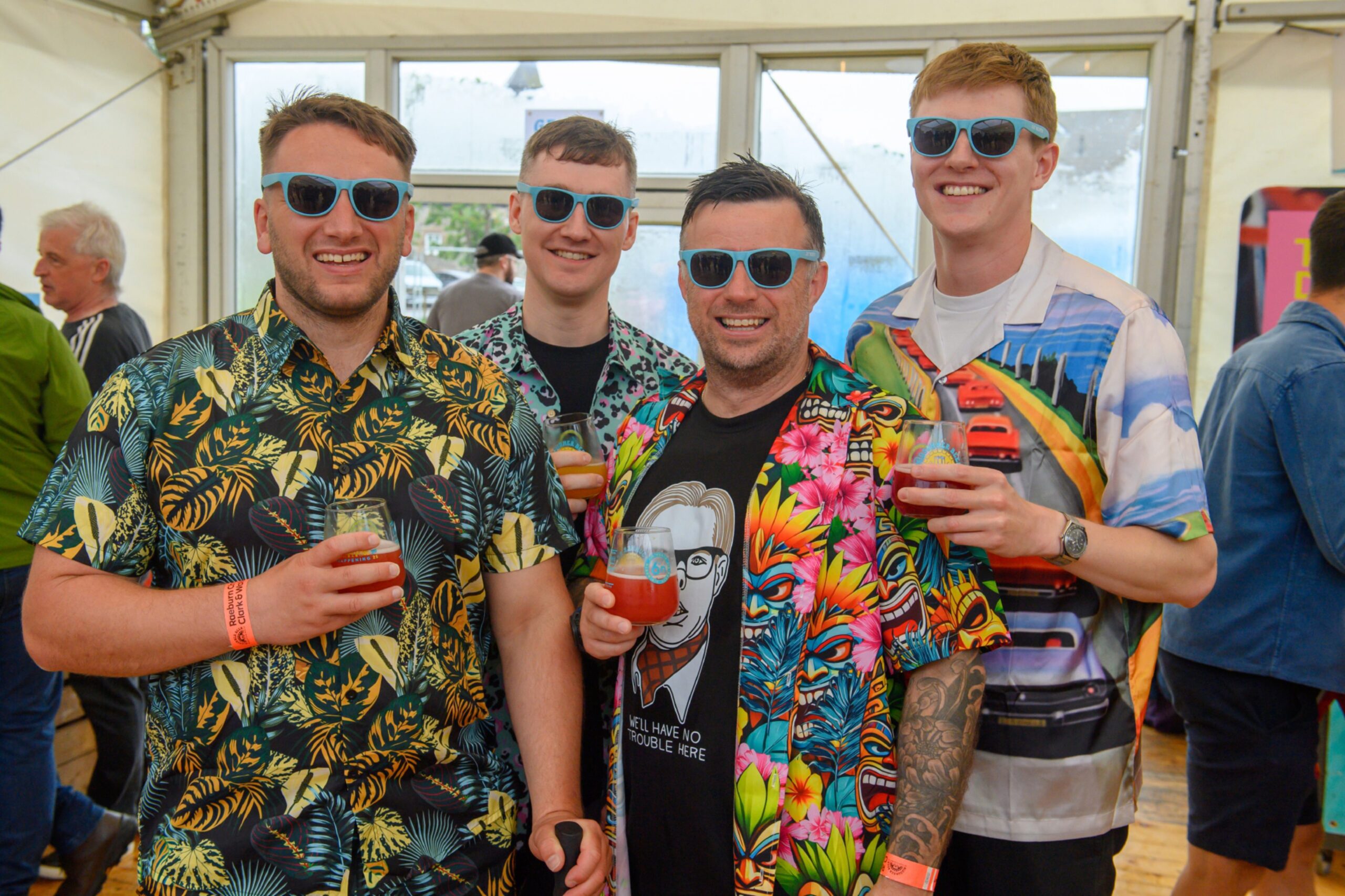 Four men in Hawaiian shirts and sunglasses pose with drinks