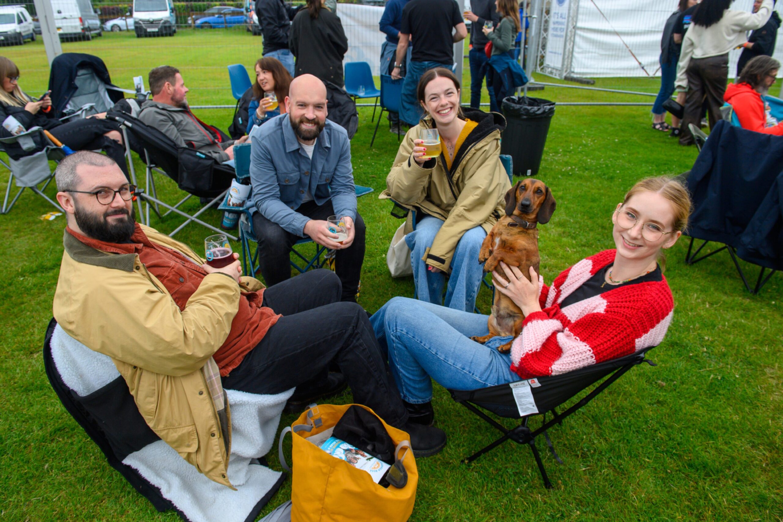 A group of four people sitting down, smiling. One has a dachshund on her lap.