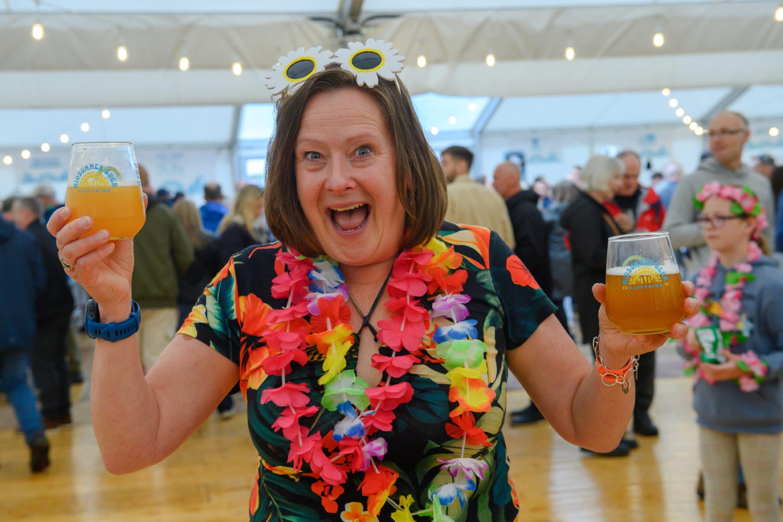 A woman in a Hawaiian shirt holds two glasses of beer