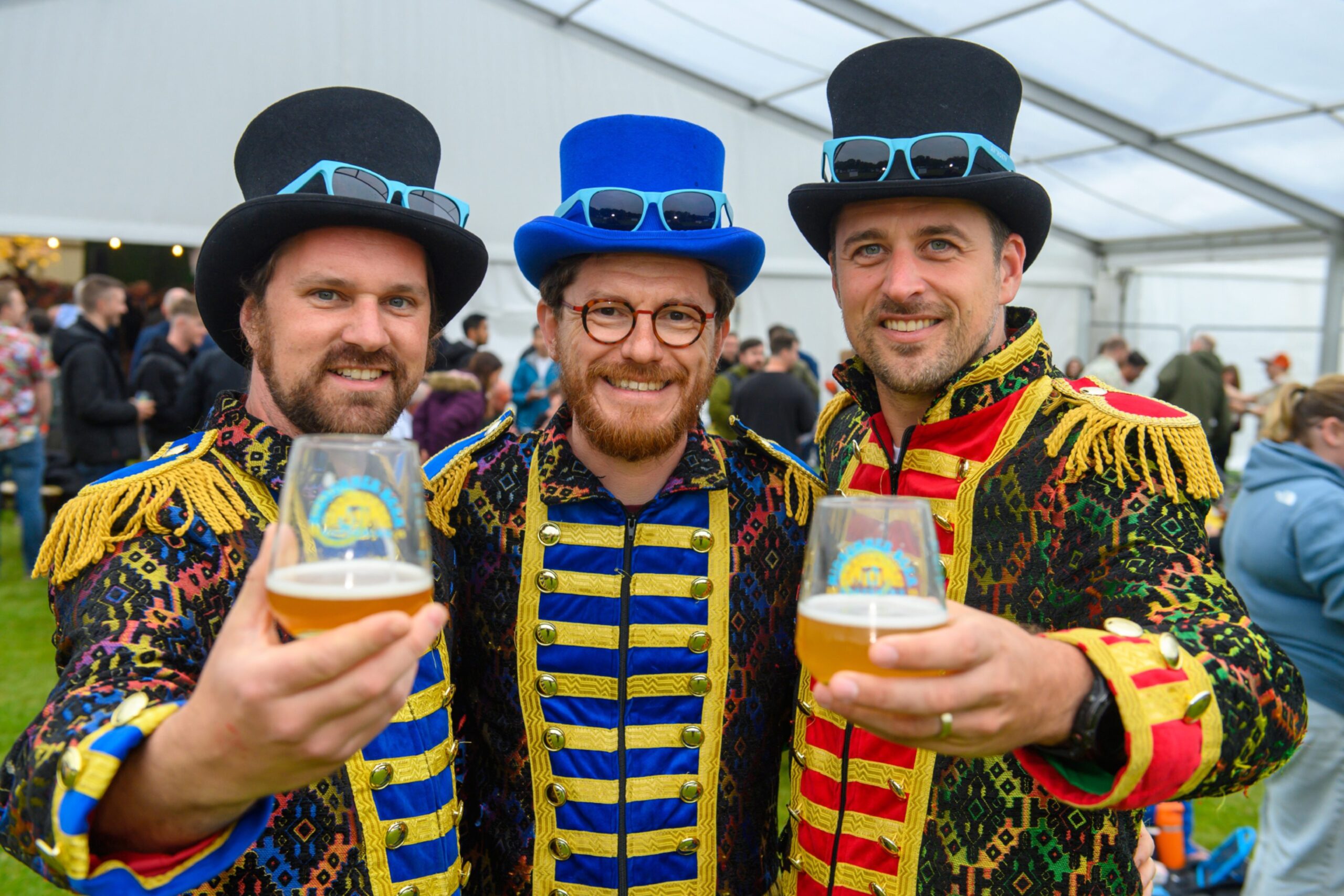 Three men dressed as circus ringmasters raise their glasses of beer