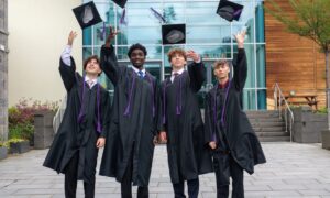 Four graduates in gowns throwing their mortar boards up in the air.
