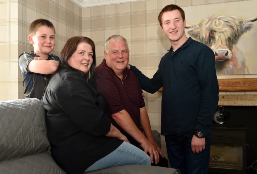 Left to right: Luke, 11, in a dark T-shirt leaning on his mum Karen's shoulder (Karen is also in a dark top. Next is Moray with his hands on one knee leaning forward and smiling. Far right is Dylon, 21, with his hand on his dad's shoulder.