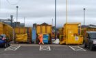 View of yellow refuse bins at the recycling centre, as a worker in orange walks in front.