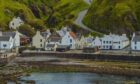 Creel cottage in Pennan, Aberdeenshire. the steep road down to the village is visible in the background.