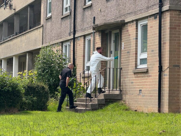 A forensics officer in white suit and police officer entering a block of flats.