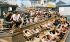 Some people stand against the railings to catch some rays while others sunbathe in deckchairs.