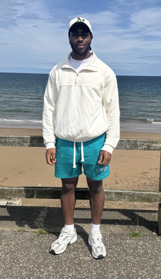 Emmanuel Akhighe at Aberdeen beach wearing teal shorts and a cream quarter-zip jumper