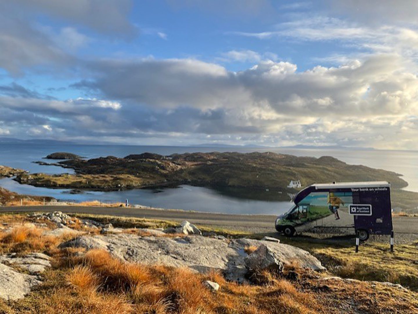 The mobile banking van driving on a road next to the sea.