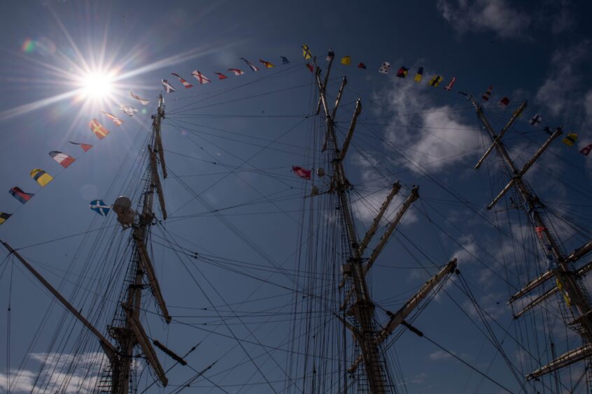 Silhouetted tall ship masts with rigging and signal flags against a bright sun and blue sky at the Tall Ships Races in Aberdeen.