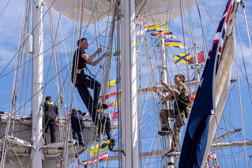 TS Royalist crew climbing the masts and rigging with colourful maritime flags in the background during the Tall Ships festival in Aberdeen.