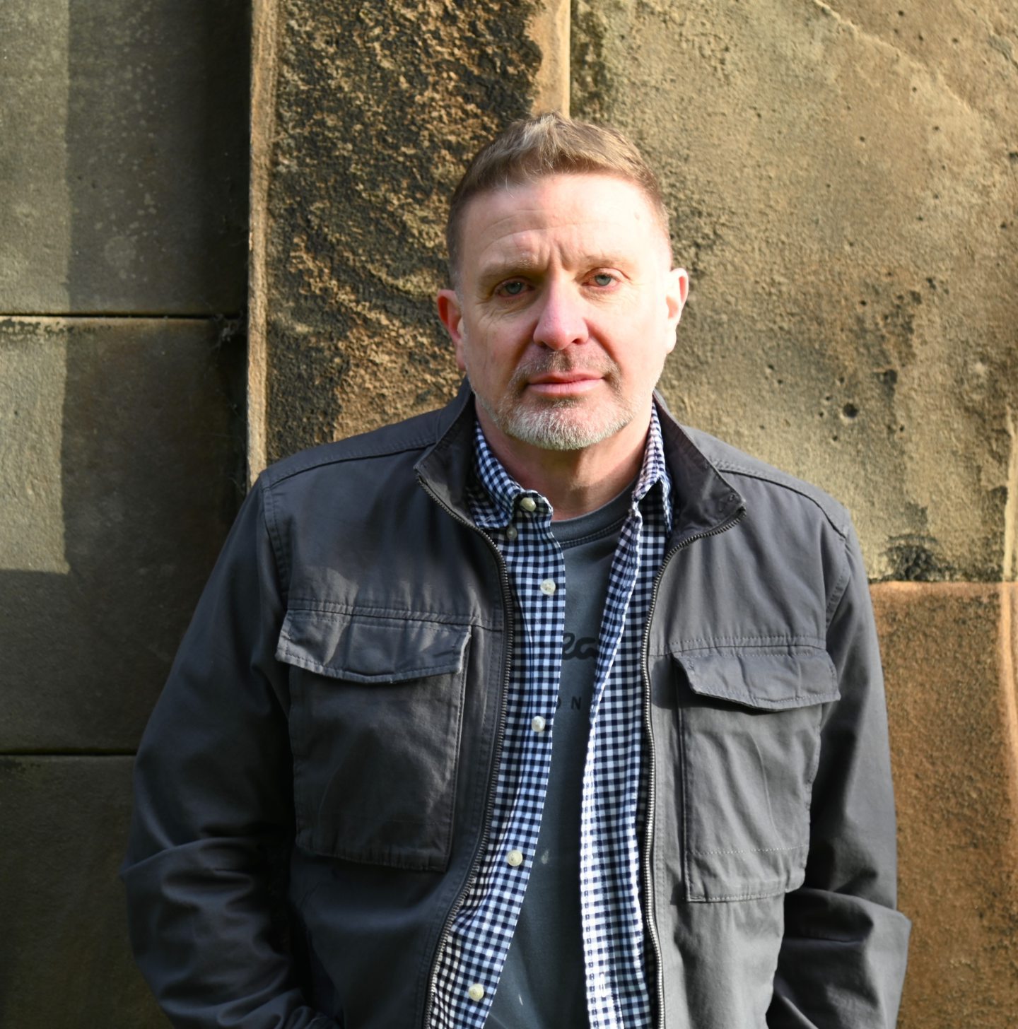 A profile photo of author Mark Bridgeman, in a dark blue jacket and blue and white checked shirt.