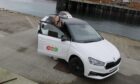 Hanna Foster standing behind the door of the white Skoda Fabia she uses to teach learners.