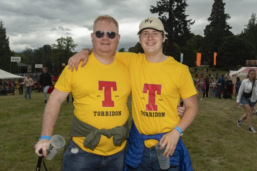 Two men in matching yellow t-shirts with the red Tennent's T on them and Torridon in smaller letters underneath.
