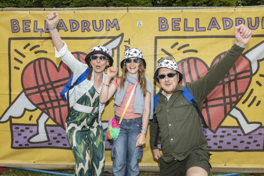Three festivalgoers in matching bucket hats stand in front of the Tartan Heart banner, with their fist in the air.