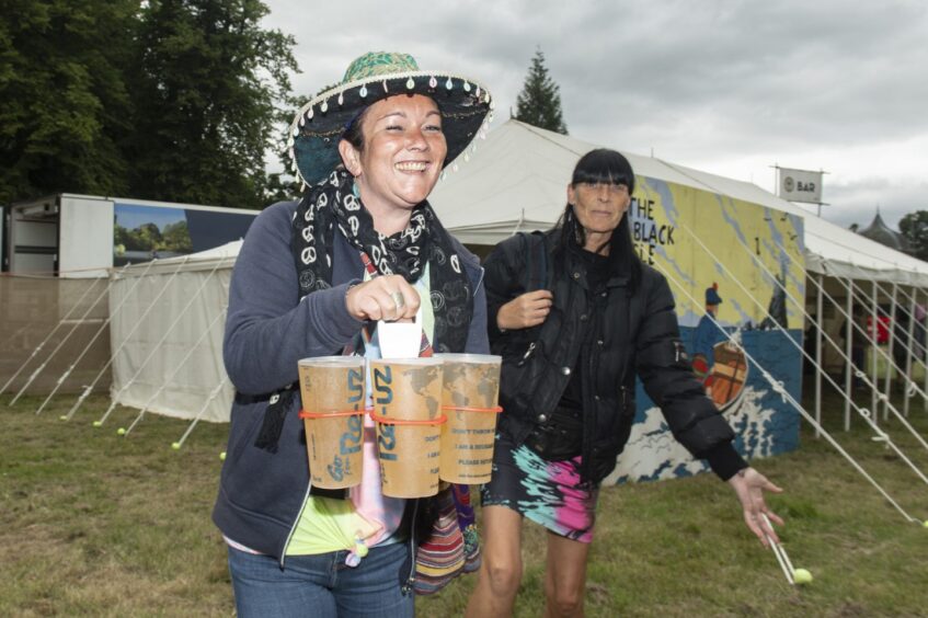 A woman in a sombrero carries three pints in a carrier while her friend looks on, just outside the beer tent.