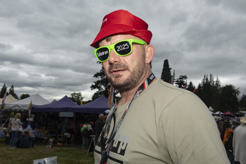 A man in plastic glasses with Belladrum 2025 written in white on them looks into the camera.