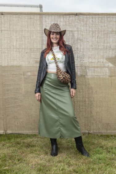 A red-haired woman wears a leopard-print Stetson, bag and leather jacket, skirt and long black boots.