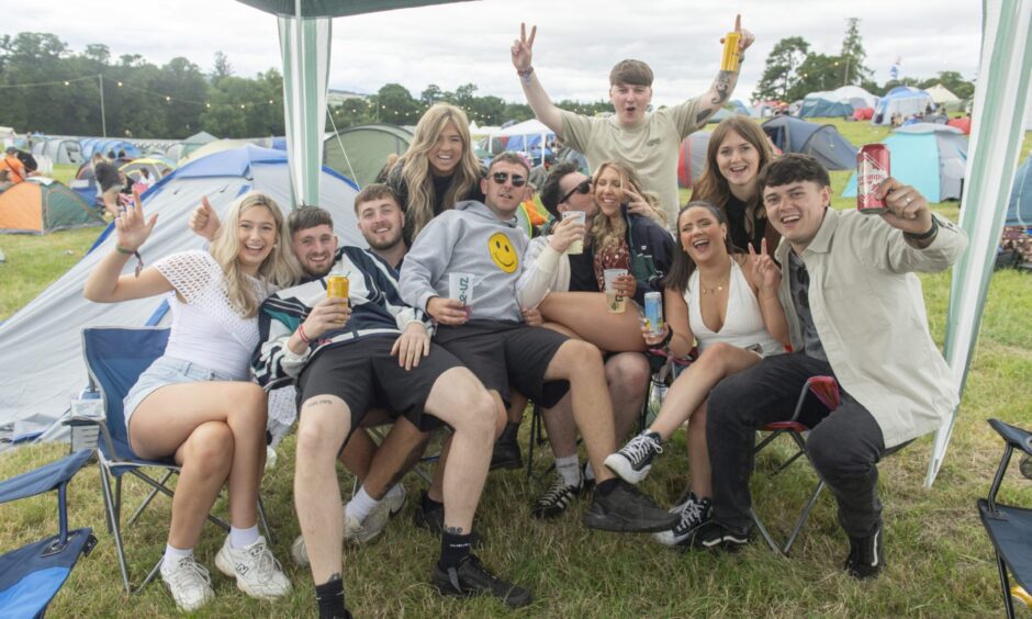 A large group of friends hold their hands and drinks in the air and smile for the camera.