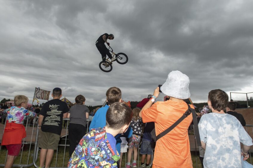 A man on a bike jumps high over the heads of the watching youngsters.