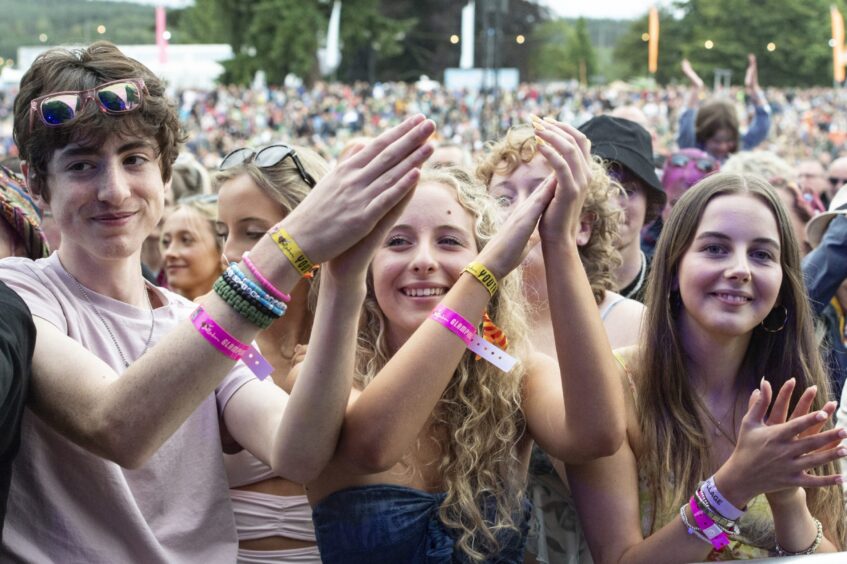 A group of young people smile at the camera from the front row of the crowd at Belladrum.