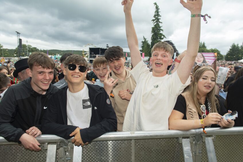 A group of young lads smile at the camera from behind the barrier in front of the stage.