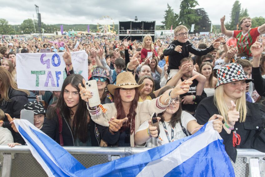 A huge crowd, with youngsters on parents' shoulders, gathers at the stage, the front row holding a saltire over the barrier.